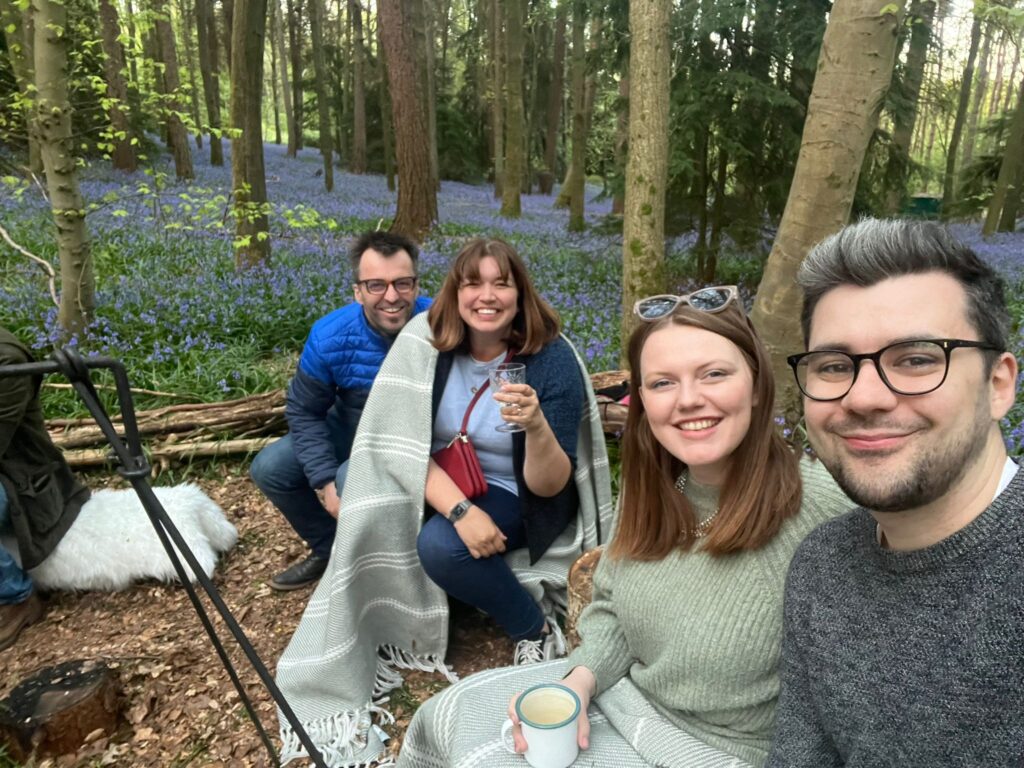 Shared experiences - 4 people sat around a fire in a woodland, surrounded by bluebells