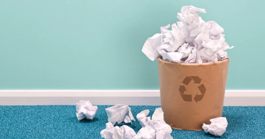 A pile of scrunched up paper in and around a recycling bin - illustrating the need for the event industry to do more about sustainability