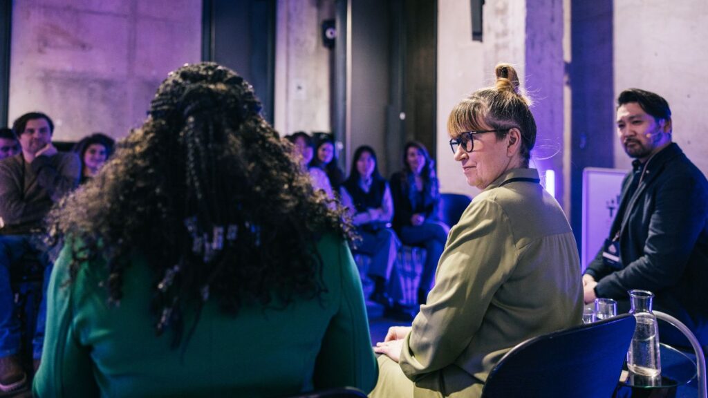 Picture of three people sat down in a discussion at an event with an audience.