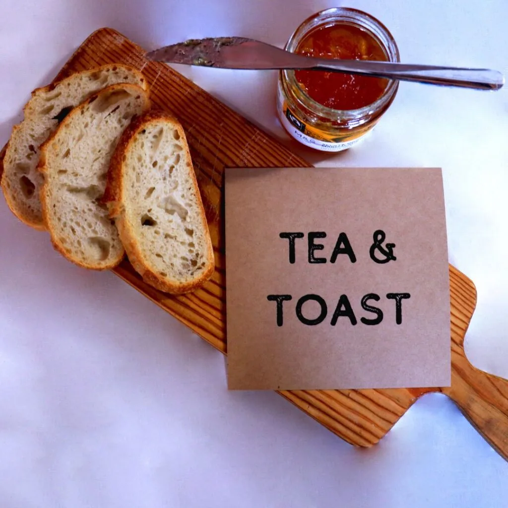 Image of a Tea&Toast flyer on a breadboard with sliced bread, a pot of marmalade and a butter knife