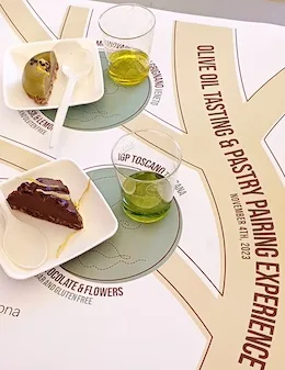 An image of 2 small cups with 2 types of olive oil in and 2 accompanying pastries, as part of an olive oil tasting activity at an event