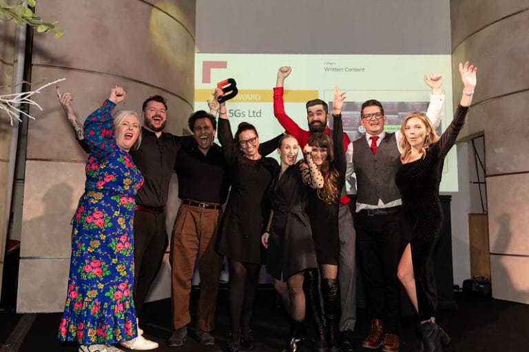 Large group of people proudly holding their BIMA award on stage, some punching the air in delight